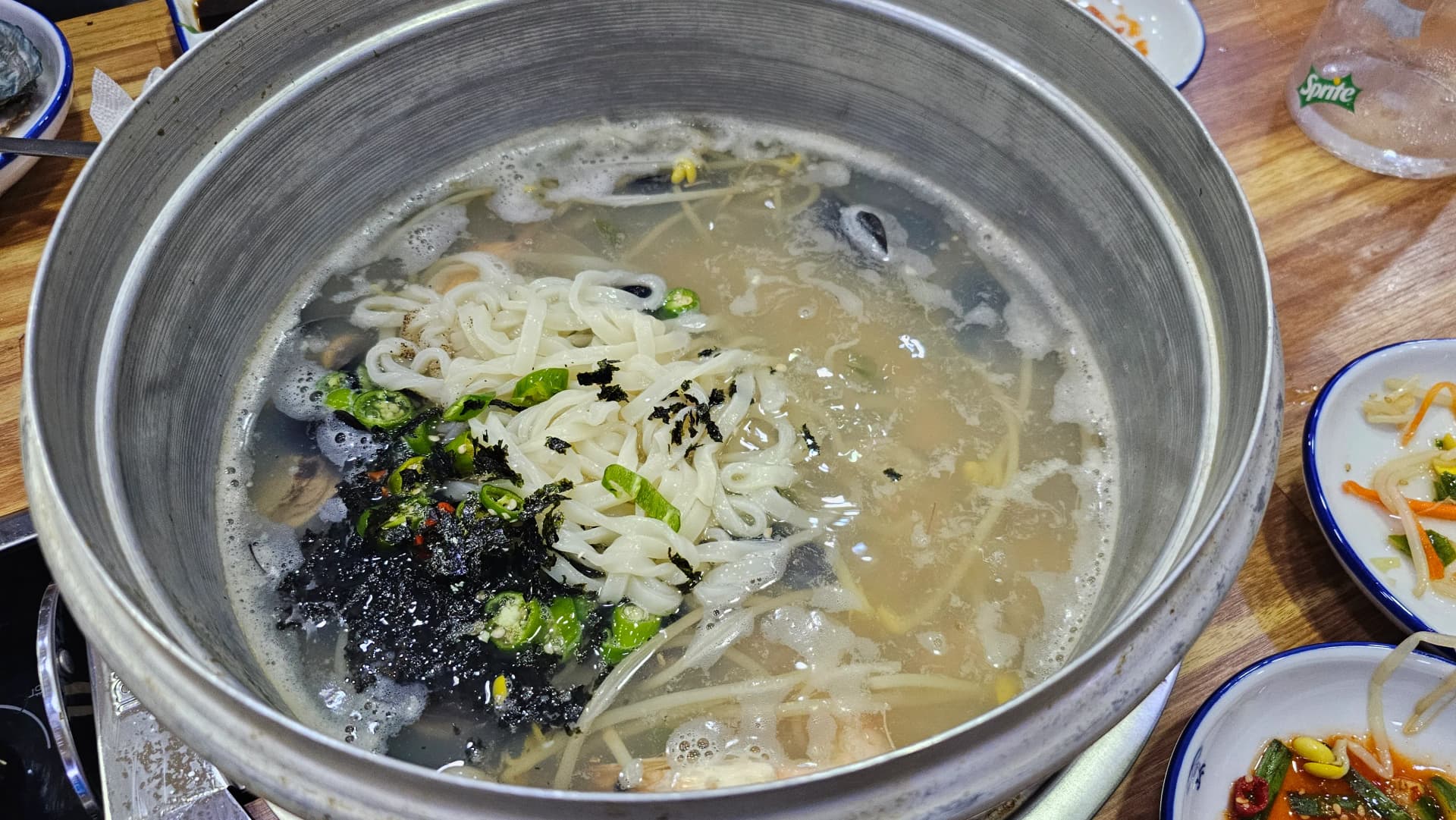 Caldo de mariscos del nivel más bajo con fideos kalguksu cocinándose, decorado con alga nori y ají picante
