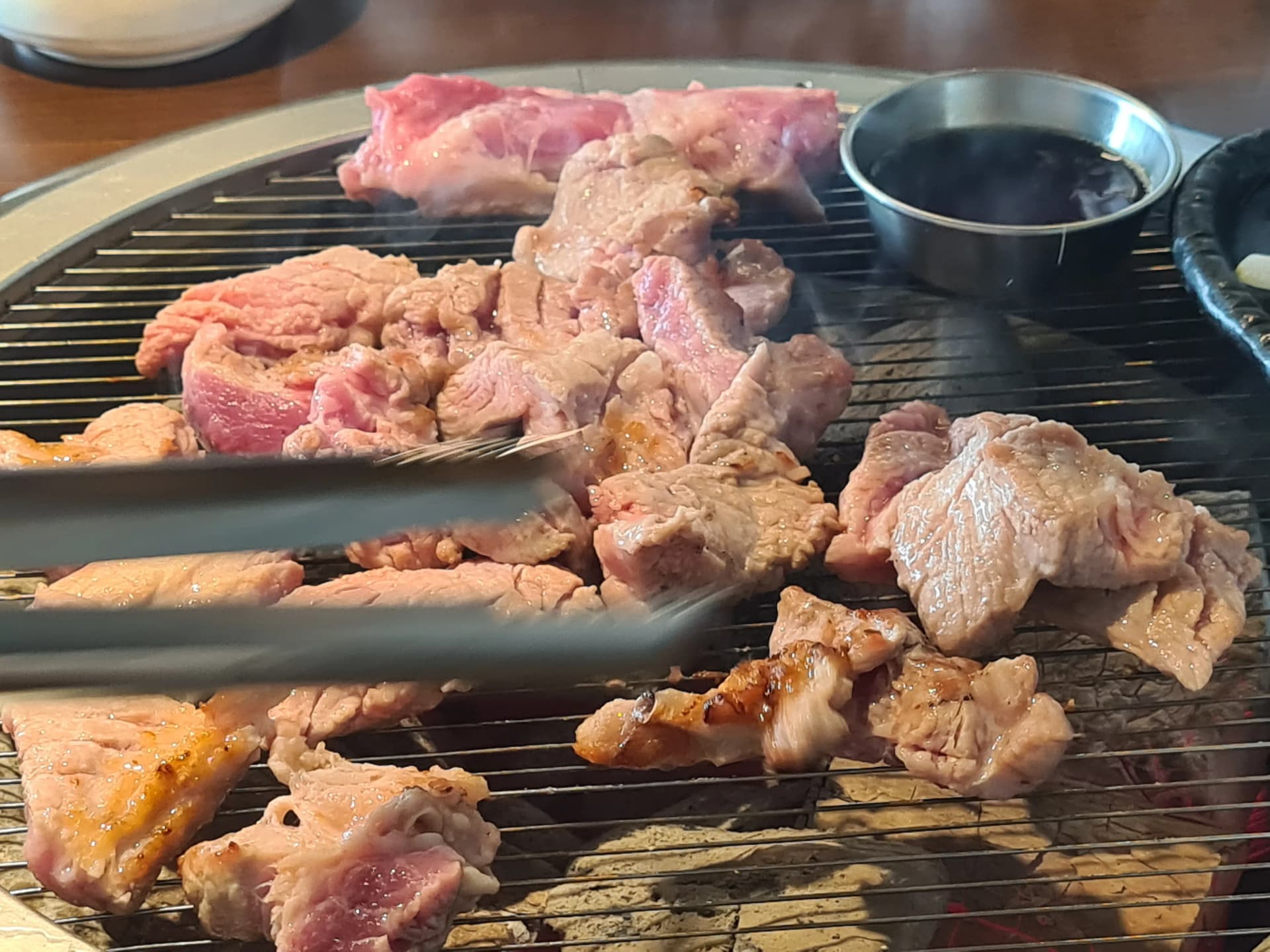 موظف المطعم يقلب ريش اللحم بملقط على شبكة الفحم — خدمة شواء كورية مساعدة