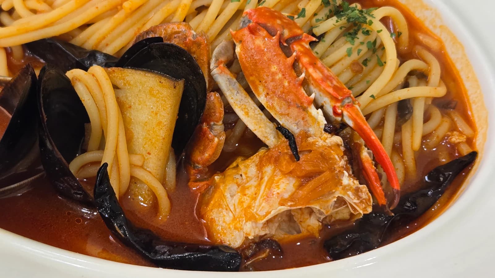 Close-up of seafood jjamppong pasta showing mussel shells and crab pieces