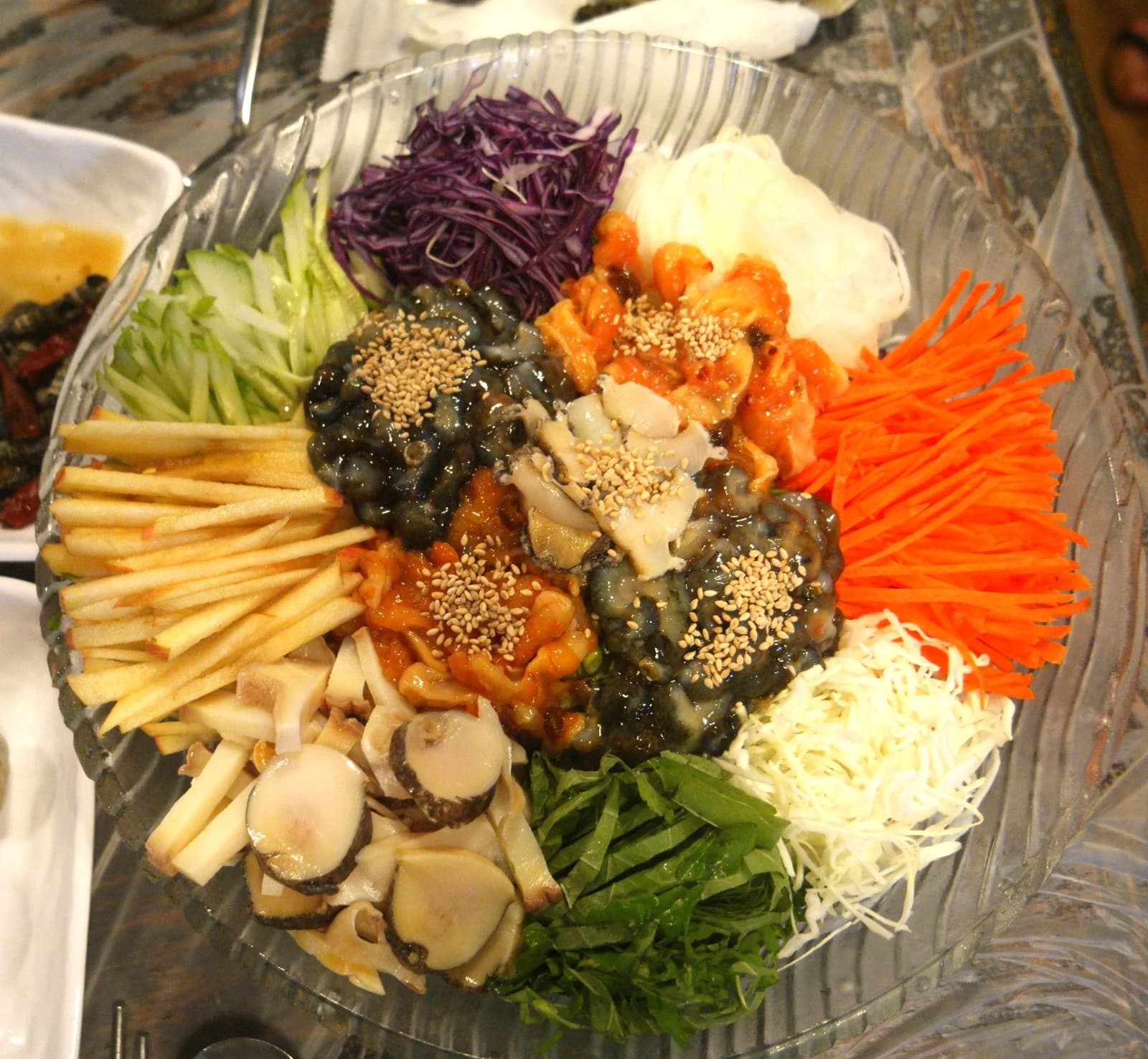 Full mulhoe bowl in a glass dish with colorful vegetables and seasoned raw seafood