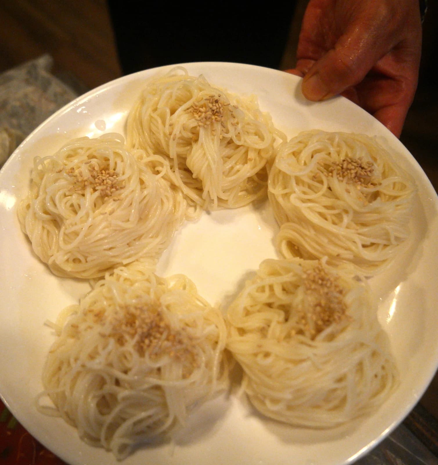 Thin wheat somyeon noodles rolled into bite-sized portions on a plate with sesame seeds