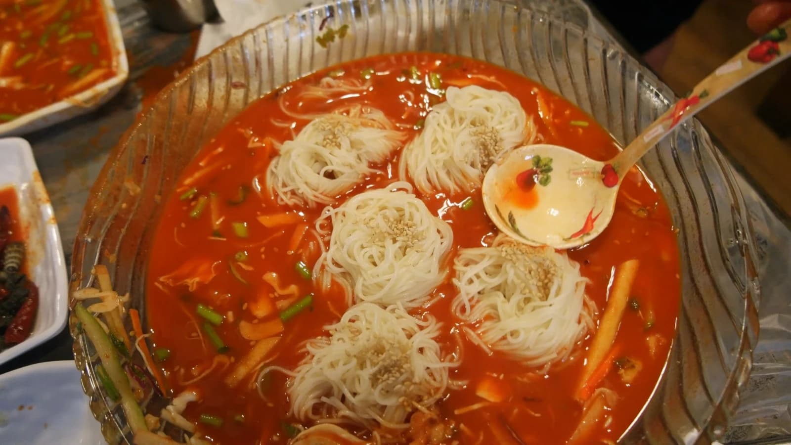 White somyeon noodles floating in red mulhoe broth before mixing