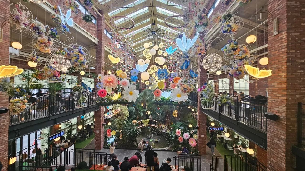 포레스트 아웃팅스 일산 본점 1층에서 올려다본 천장 꽃 조형물과 나비 장식, 조명이 가득한 실내 전경 | 하이제이에스비