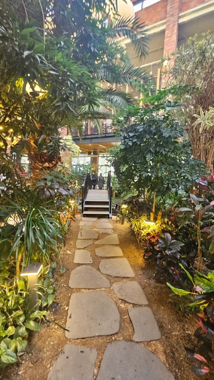 포레스트 아웃팅스 1층 돌길 산책로 양쪽으로 빽빽한 열대식물과 끝에 보이는 계단 | 하이제이에스비
