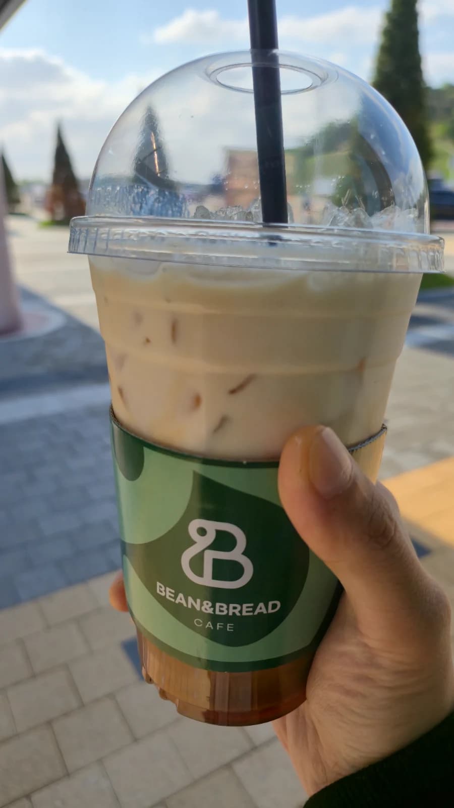 Iced vanilla latte in clear cup with green sleeve and Bean and Bread cafe logo
