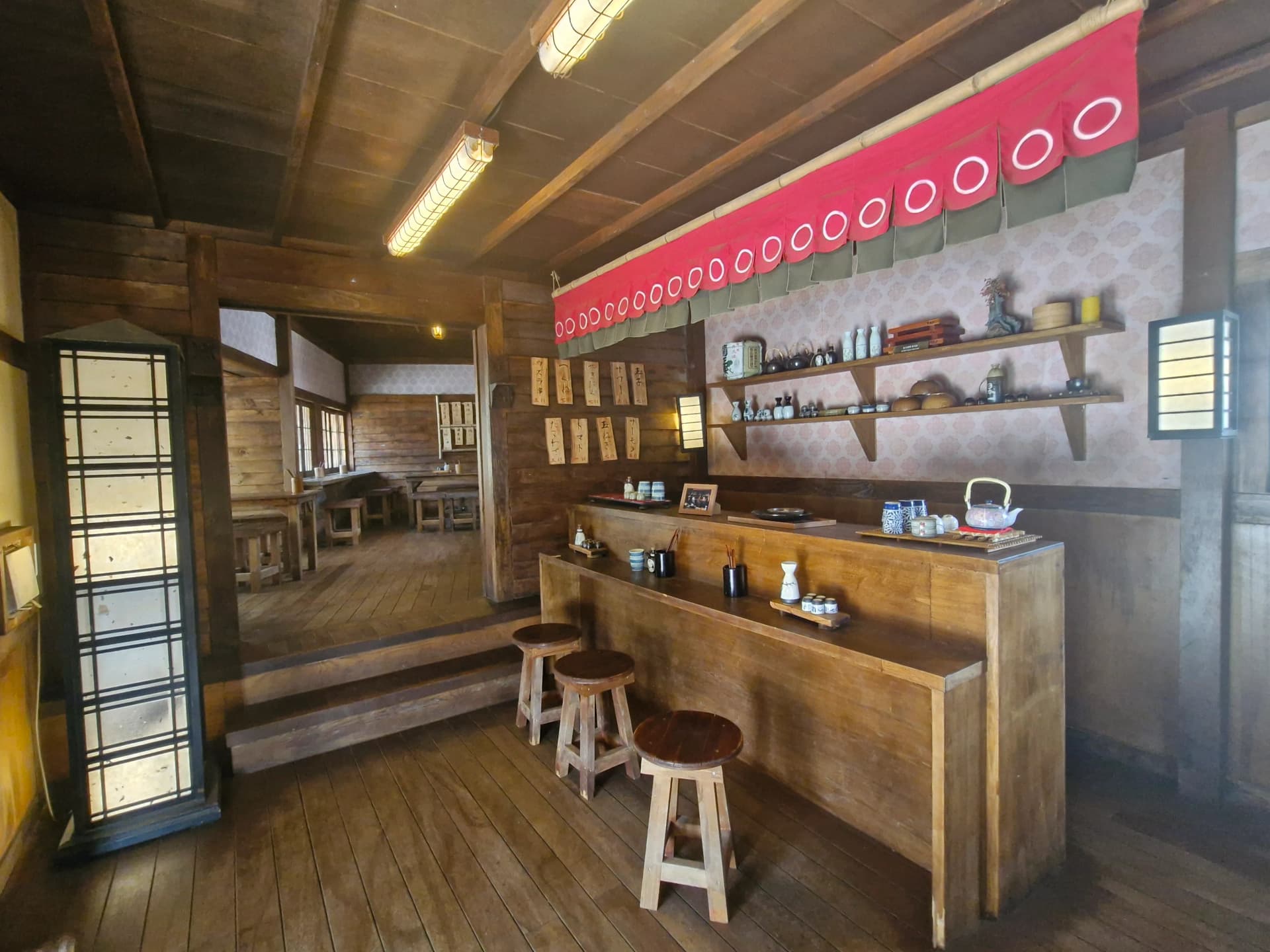 Bangku kayu berjejer di bawah noren merah di dalam kedai sake | 하이제이에스비