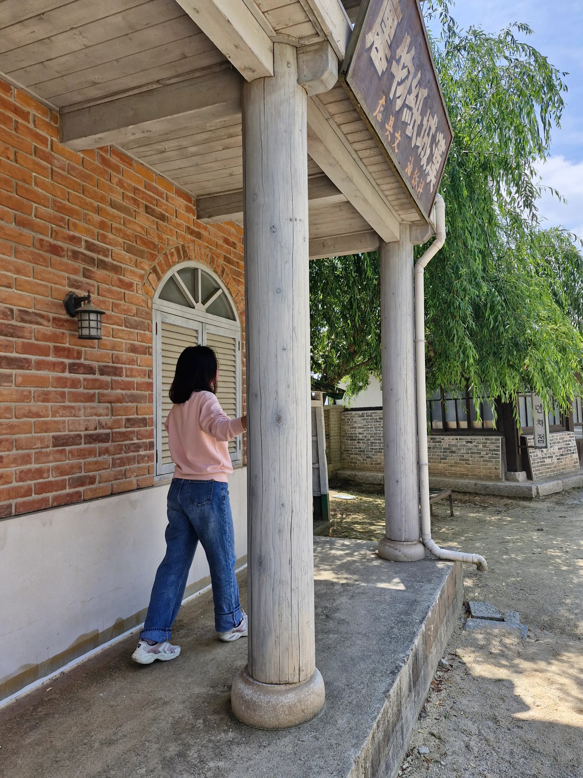 Pengunjung berdiri di depan pilar bata merah dengan papan nama aksara Cina | 하이제이에스비