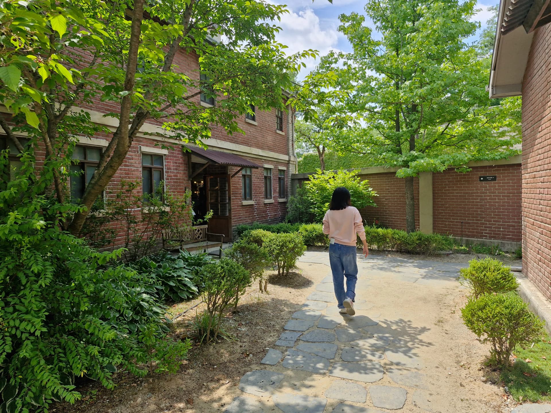 Jalan batu menuju halaman dalam bangunan bata merah dengan taman bunga | 하이제이에스비
