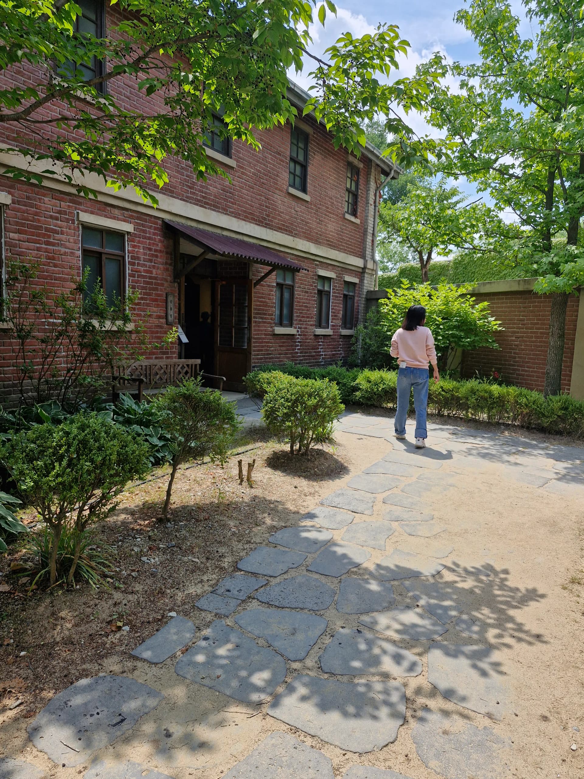 Tampak dekat jalan batu dengan dinding bangunan, taman, dan bangku jendela | 하이제이에스비