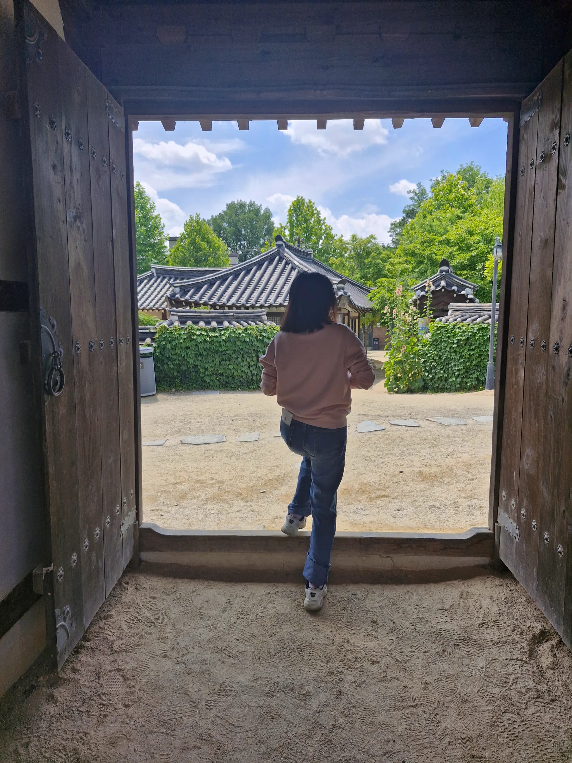 Halaman hanok terlihat melalui celah gerbang kayu besar | 하이제이에스비