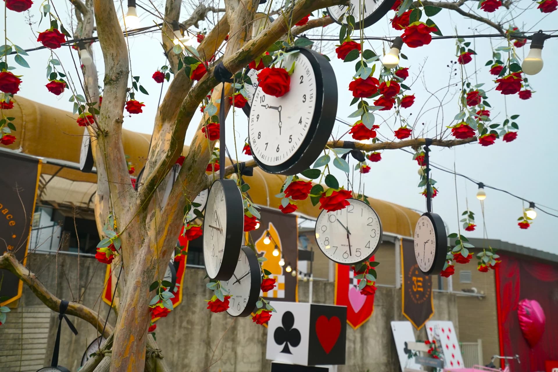 Clock tree in the garden with dangling timepieces and red roses woven through the branches