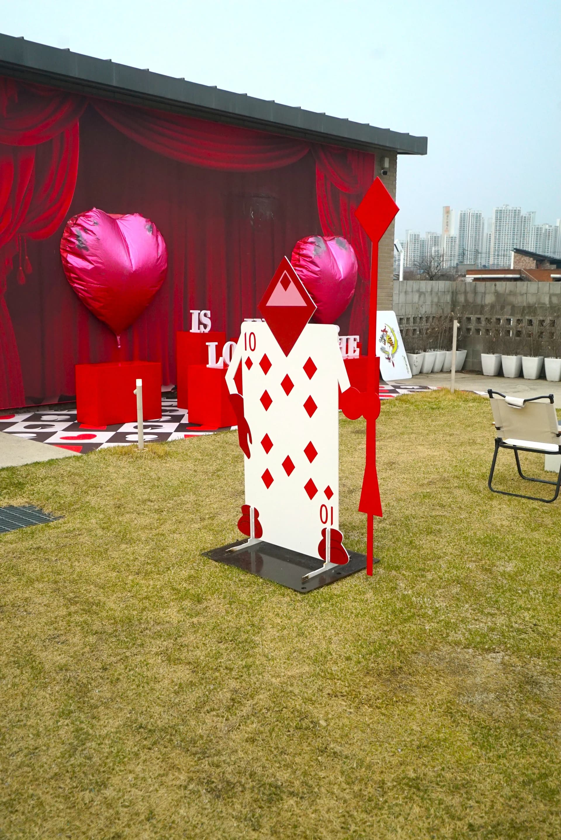 Red curtain stage with pink heart balloons creating a photo zone at 3Cheon Village
