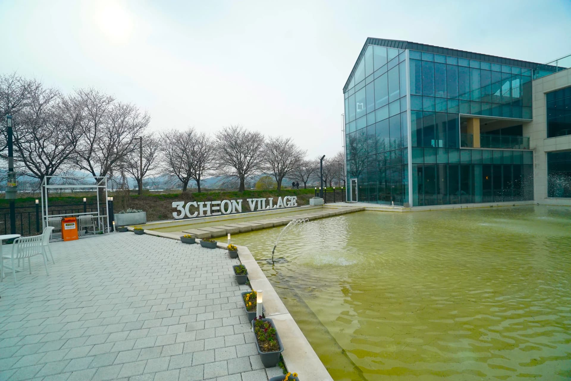 Fountain plaza with a pond and water feature next to the glass-walled building at 3Cheon Village