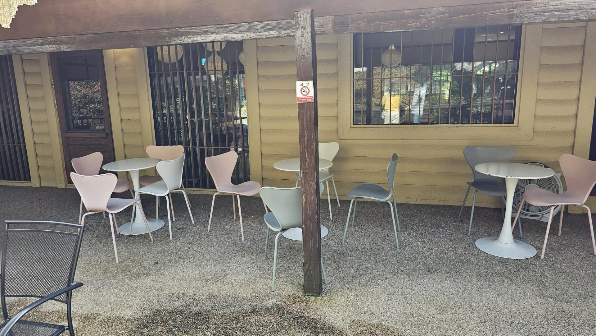 عمارت کے ساتھ موجود آؤٹ ڈور نشستیں، پیسٹل رنگ کی کرسیاں اور لکڑی کی دیوار