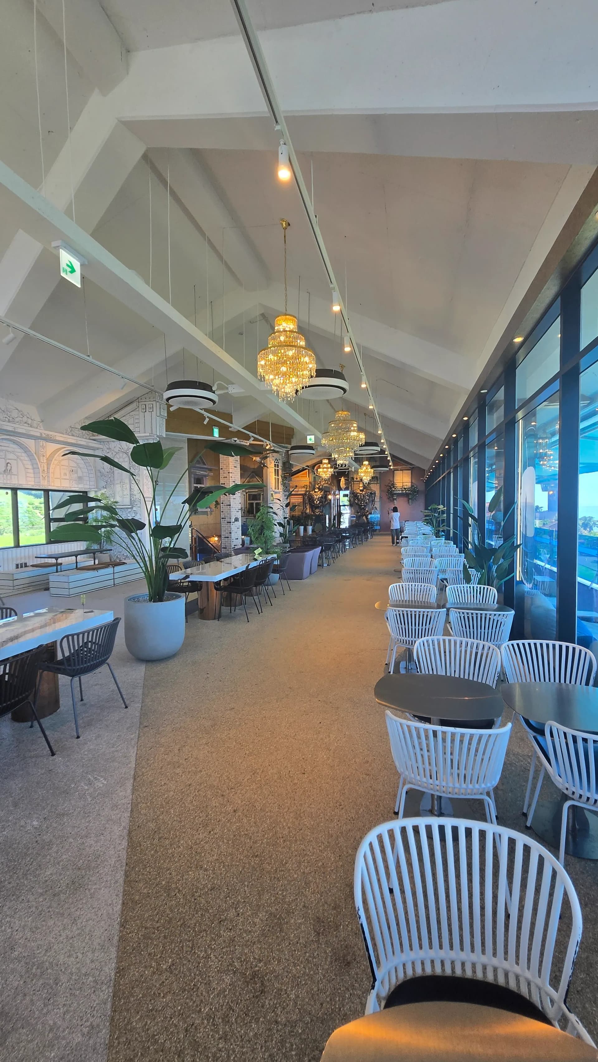 더킹 카페 오션뷰 홀 반대편 앵글 - 흰색 의자 라인과 샹들리에 반복 배치 - The King Cafe ocean view hall opposite angle with white chairs and repeated chandeliers | 하이제이에스비