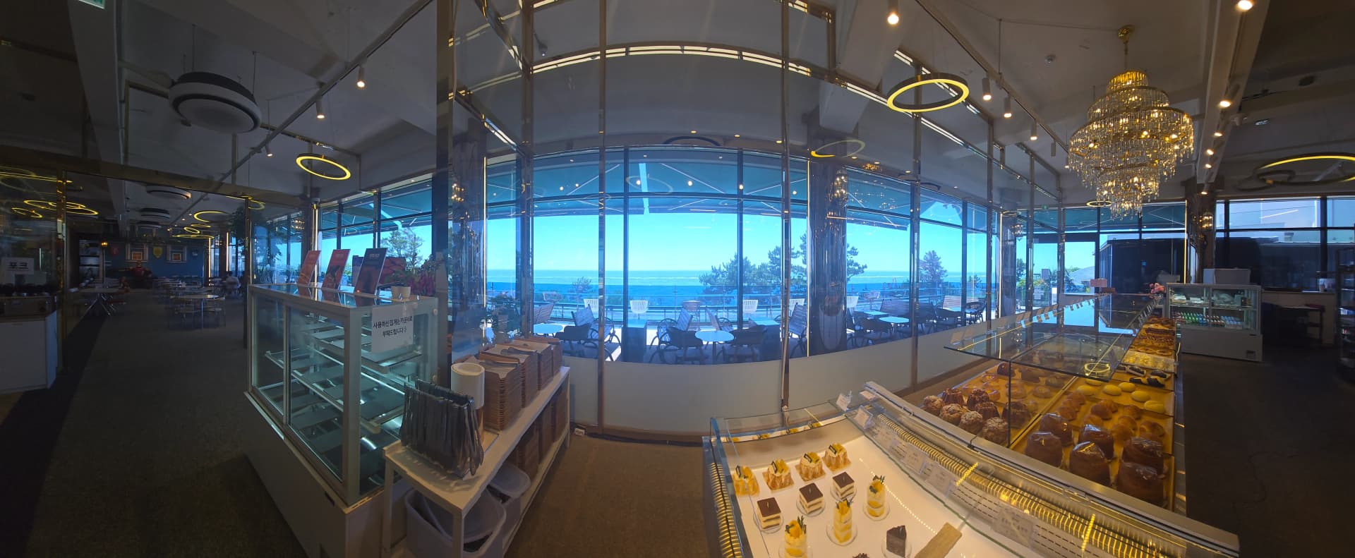 더킹 카페 주문 카운터 베이커리 진열대 너머로 보이는 동해 바다 곡선 유리창 - The King Cafe ordering counter and bakery display with curved ocean view window behind | 하이제이에스비