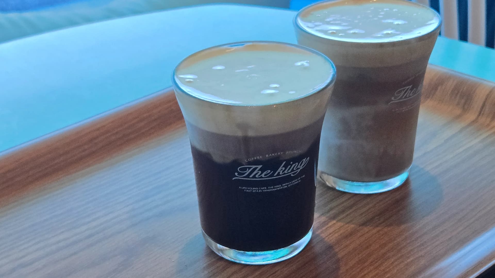 더킹 카페 시나몬크림라떼 아이스 - 연한 색 크림 층 The King 로고 유리잔 바다 배경 - The King Cafe Cinnamon Cream Latte iced with light cream layer in logo glass with ocean background | 하이제이에스비