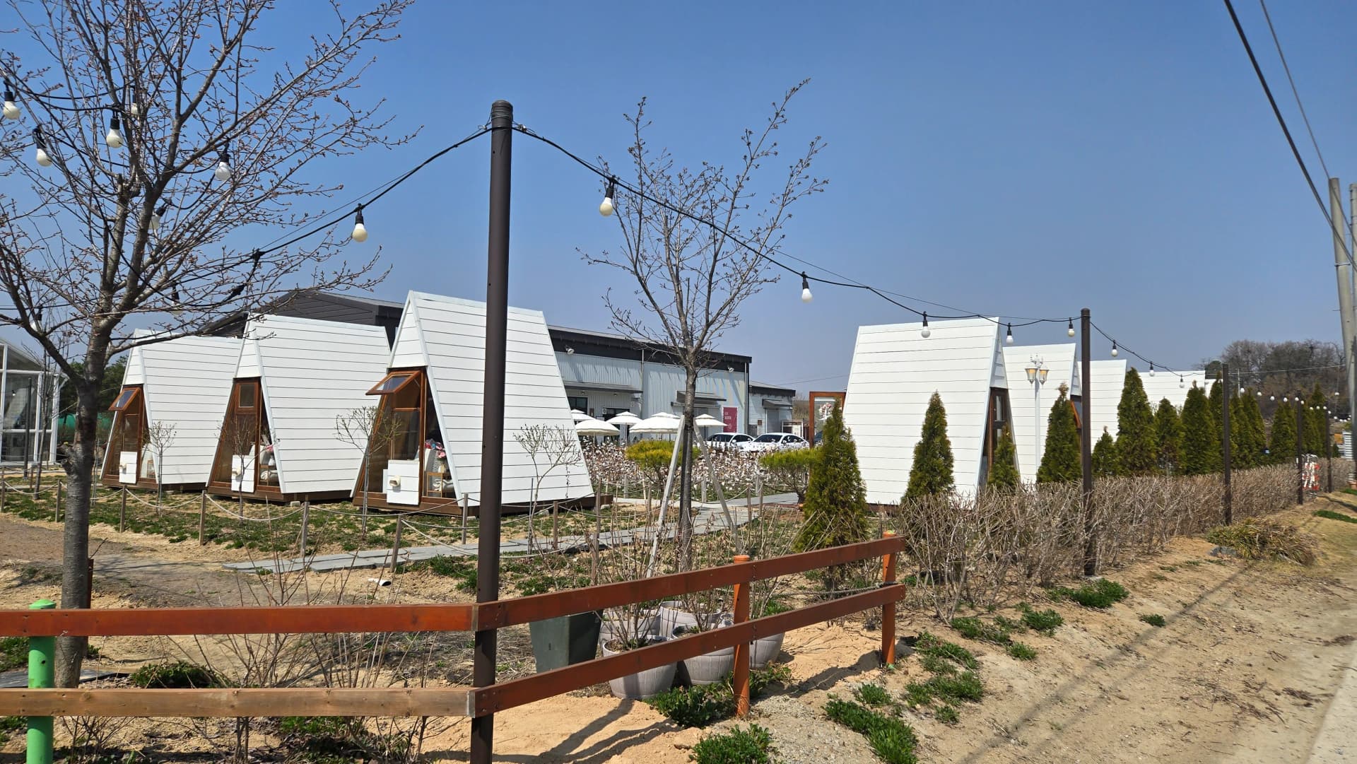 Panoramic view of Toseong Village garden cafe with A-frame timber cabins lined up along the garden path
