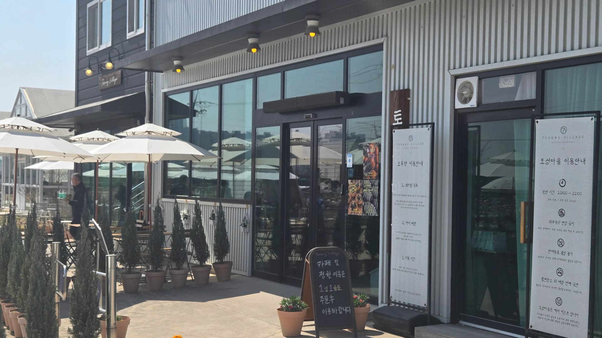Entrance to the main building at Toseong Village with chalkboard sign and opening hours on the glass door