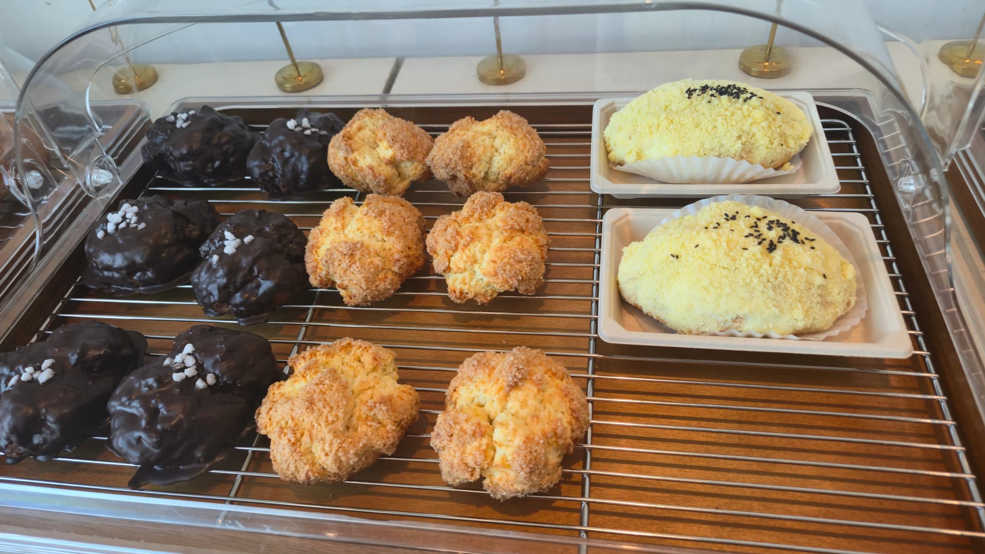 Bakery display trays with chocolate-coated bread topped with pearl sugar and assorted crumble buns