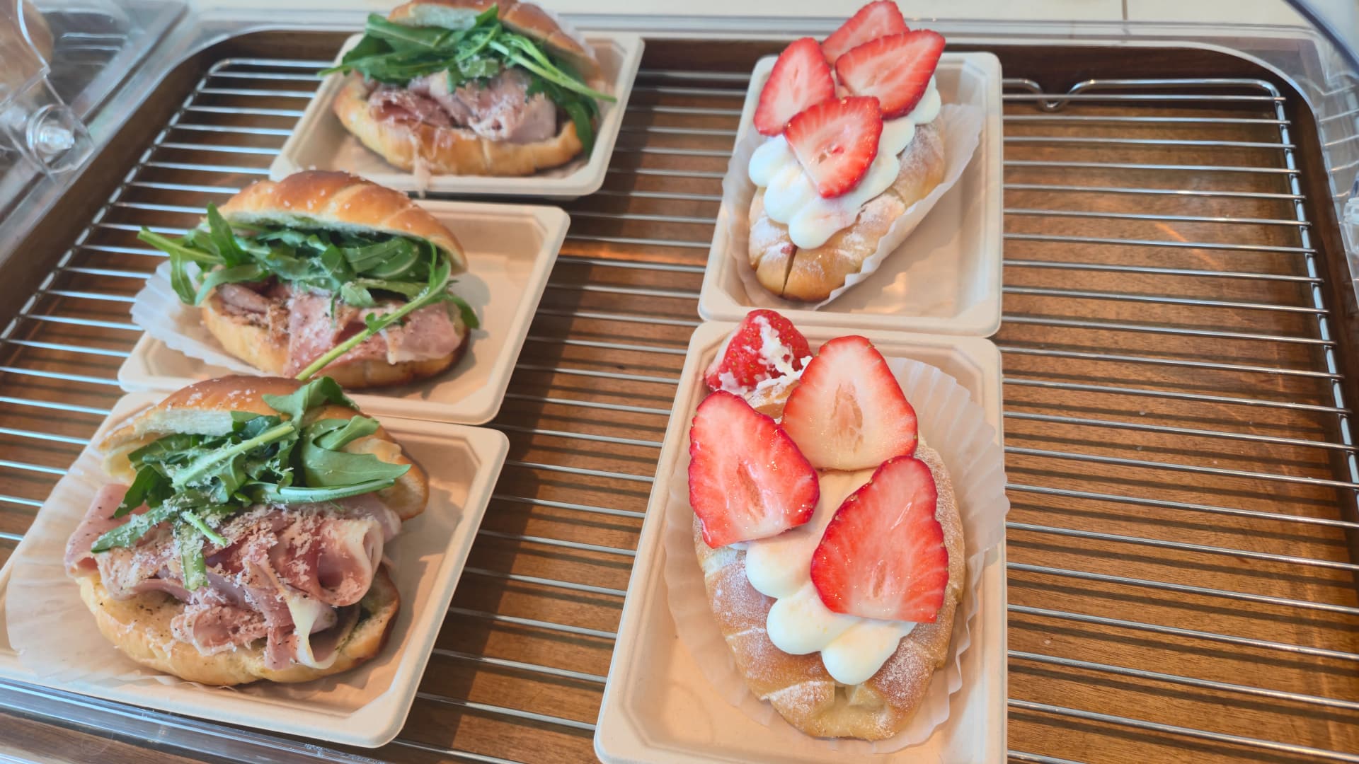 Prosciutto and rocket sandwich next to a strawberry cream open sandwich on the bakery display