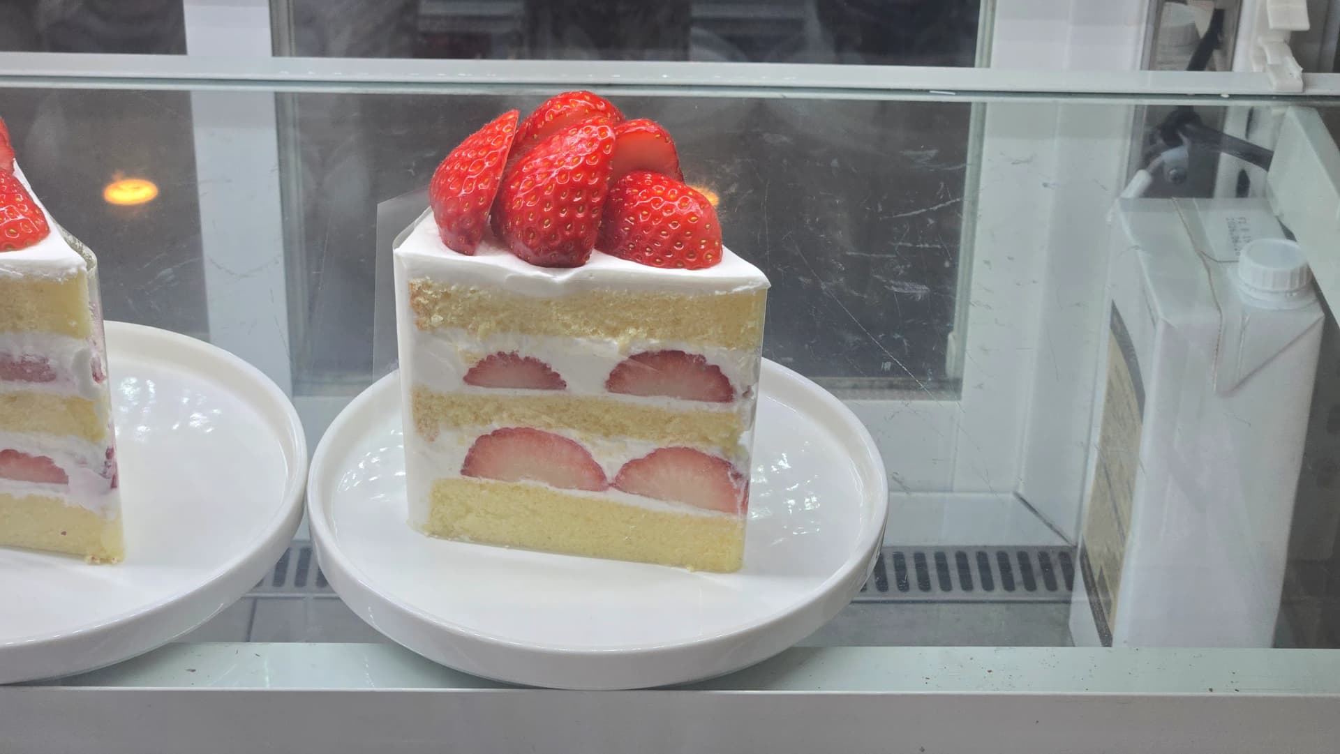 Strawberry fresh cream cake in the refrigerated showcase with halved strawberries layered between sponge