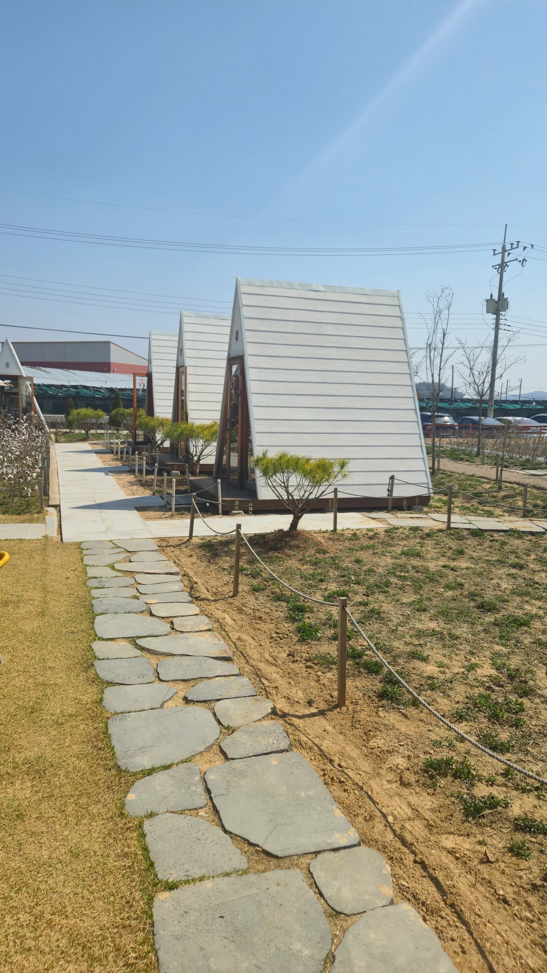Interior of a triangular-roofed cabin at Toseong Village with timber floor cushions and the garden visible through the open door