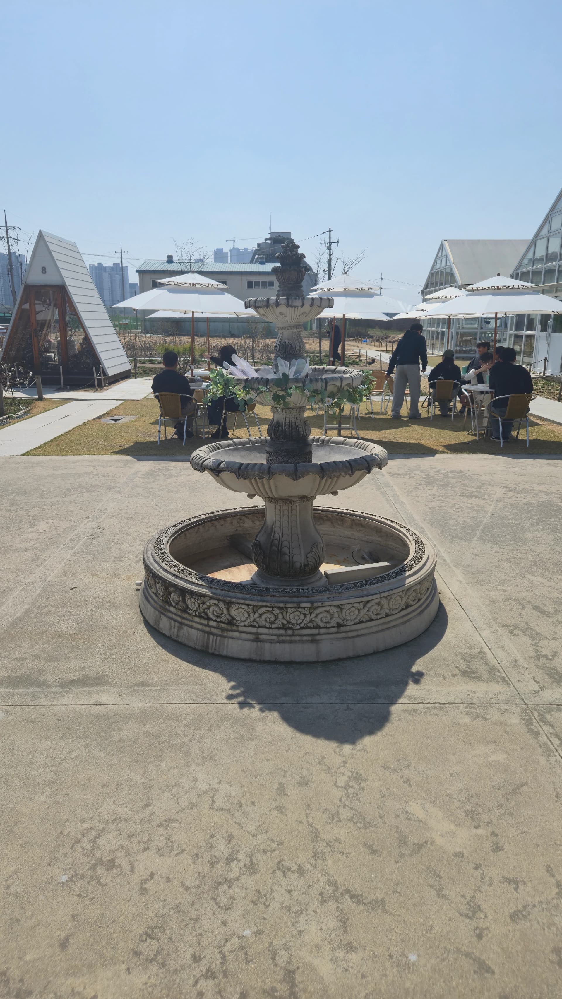 European-style three-tiered fountain in front of the main building with outdoor seating, A-frame cabins and greenhouse behind