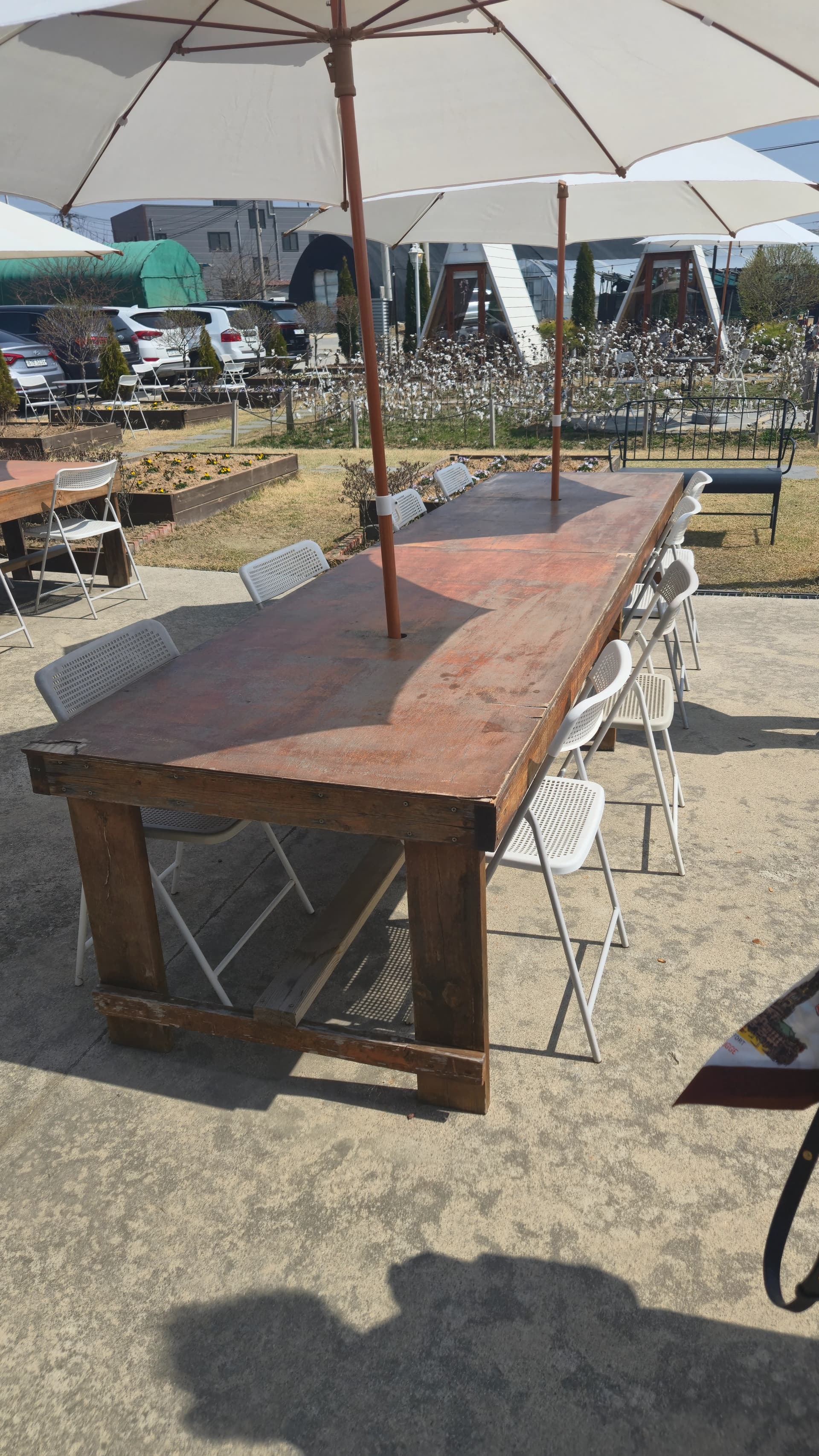 Three-metre-long timber table next to the fountain with two umbrellas and white chairs lined up on both sides