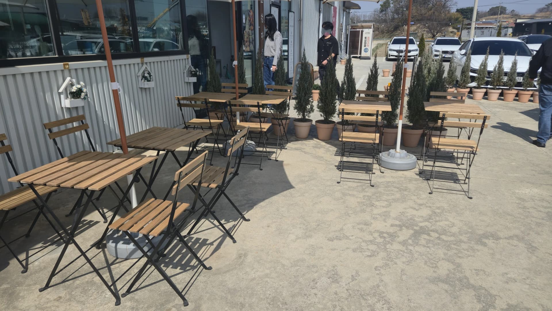 Terrace seating at the front of the main building with folding timber tables, black iron chairs and cypress planters