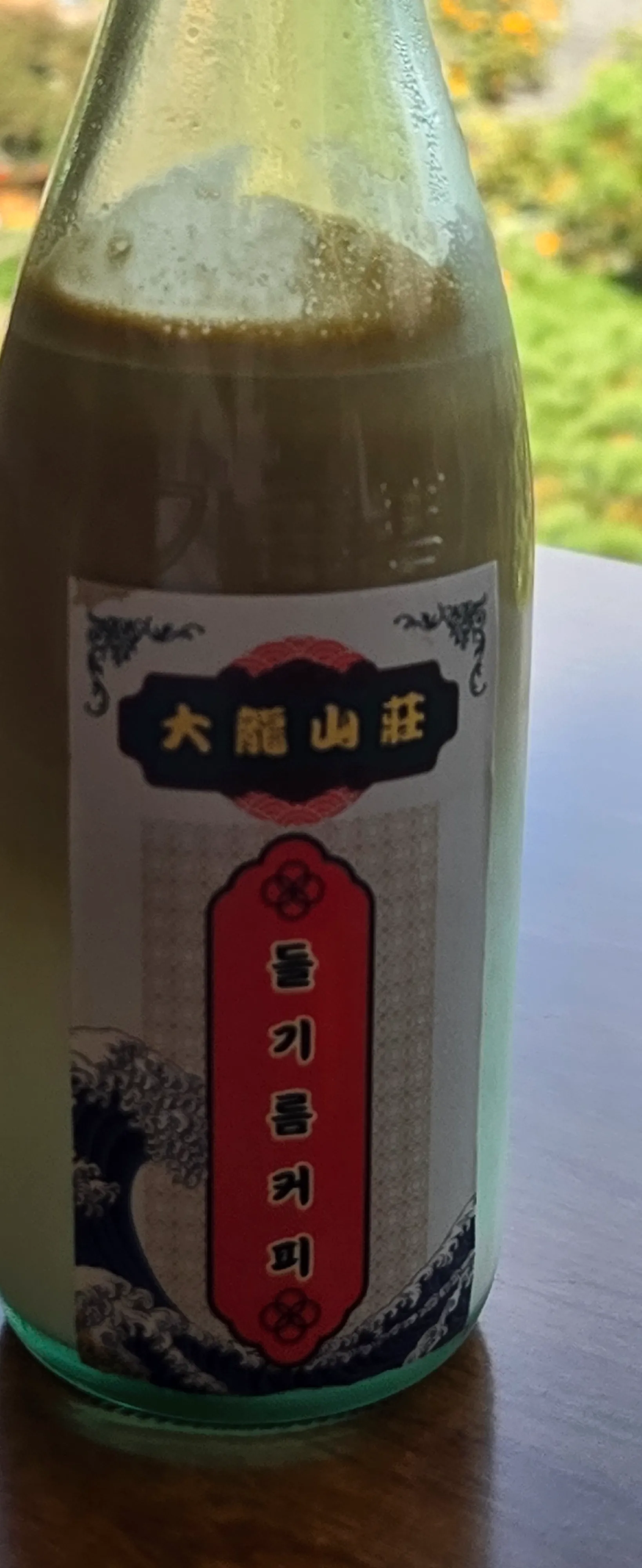 Close-up kopi botol minyak perilla, label dengan logo 大龍山莊 dan ilustrasi ombak | 하이제이에스비