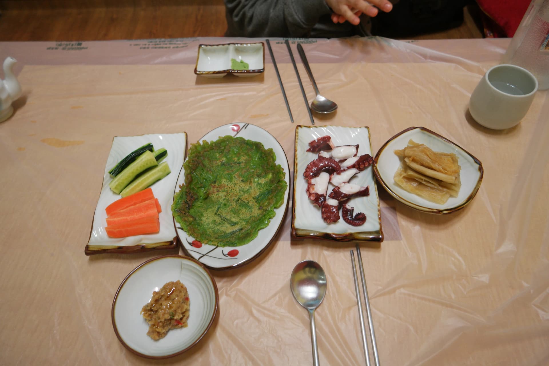 거제도 바닷가 횟집 첫 상차림 - 오이 당근 스틱, 초록빛 전, 삶은 문어, 백김치가 비닐 테이블 위에 놓여있다 | 하이제이에스비