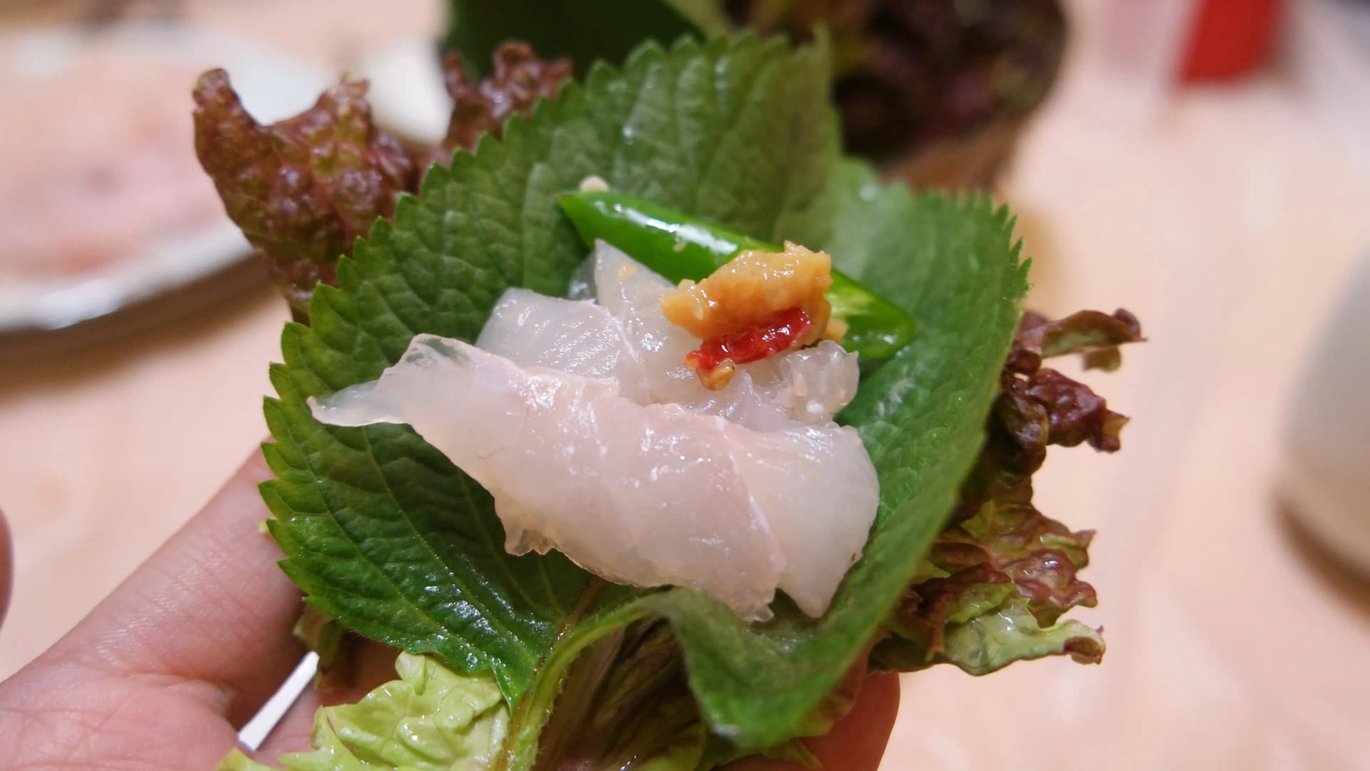 상추, 깻잎, 회 두 점, 마늘, 초장이 올려진 쌈 클로즈업 - 반투명하게 빛나는 신선한 회 | 하이제이에스비