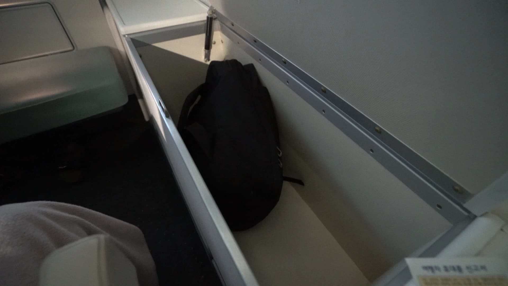 Personal storage shelf beneath the upper deck window seat on Korean Air 747-8i with room for a full backpack